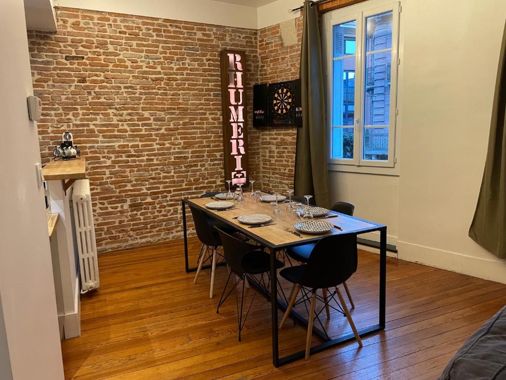 d'une salle à manger avec une table, des chaises et un mur en briques. dans l'établissement L'Étage, hypercentre Toulousain, Climatisé, à Toulouse