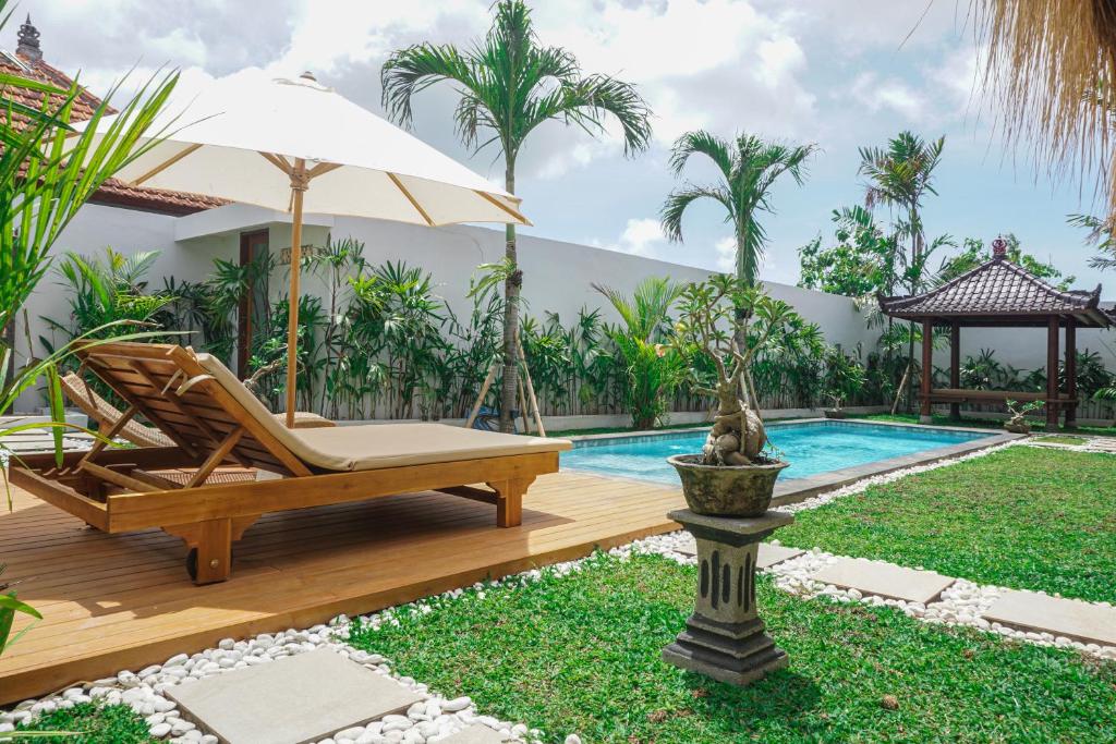 una terraza con una silla y una sombrilla junto a la piscina en Villa 10 Rose Bali 3BR Luxury en Ungasan