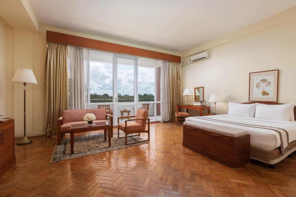 ヤンゴンにあるインヤ レイク ホテルのベッドと椅子が備わる広いホテルルームです。