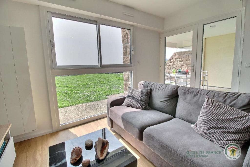 a living room with a gray couch and windows at La plage in Trébeurden