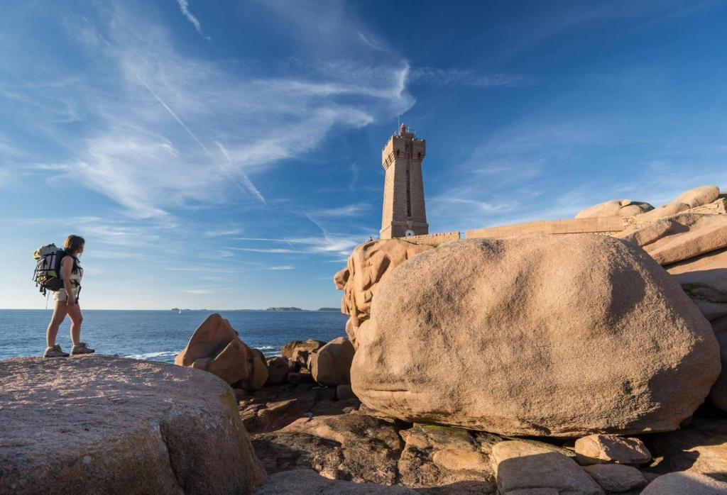 a man with a backpack standing on a rock with a lighthouse at La plage in Trébeurden