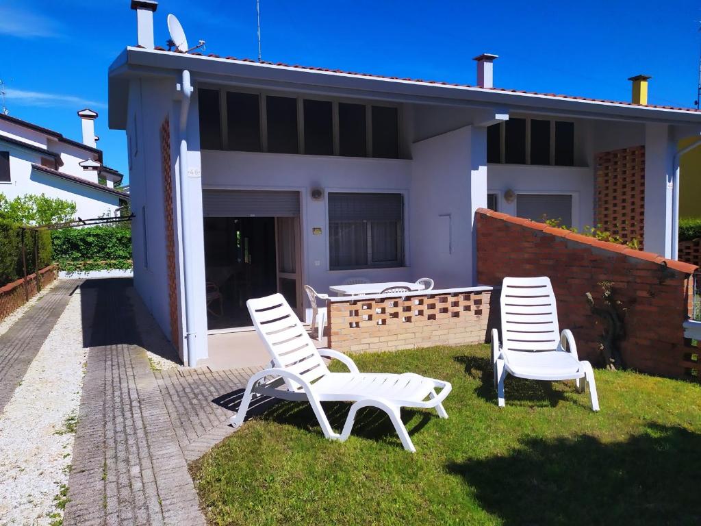 three white chairs sitting in the grass in front of a house at Bright villa with private garden - Beahost Rentals in Caorle