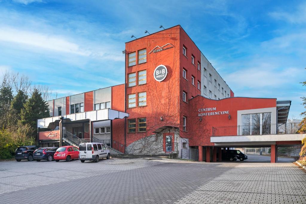 un edificio de ladrillo rojo con coches aparcados en un aparcamiento en B&B Widok en Bielsko-Biala