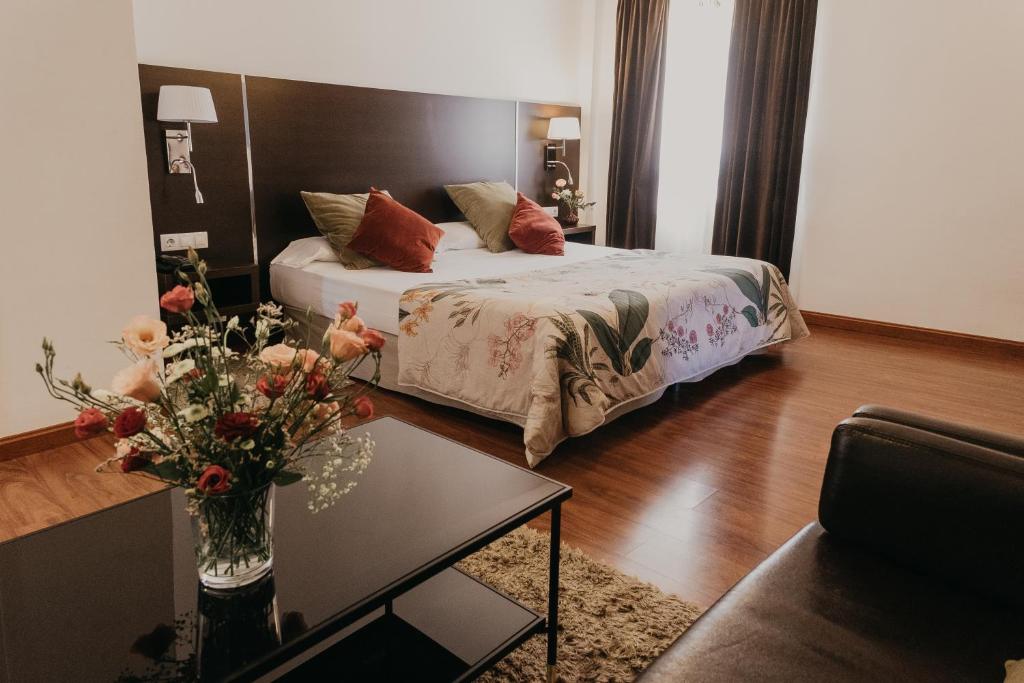 Un dormitorio con una cama y una mesa con un jarrón de flores en Mare Hotel, en Dos Hermanas