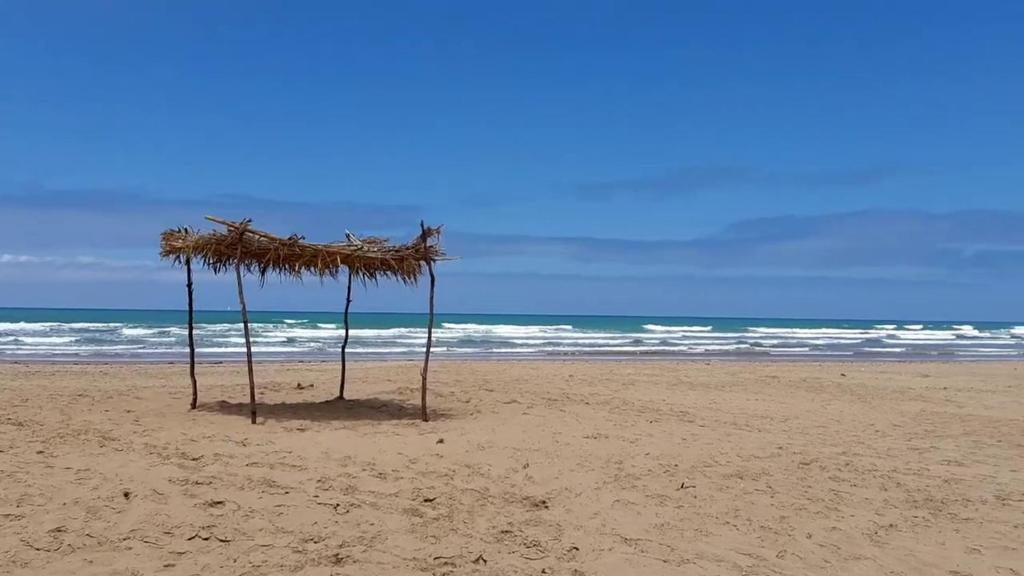 una cabaña de paja en una playa con el océano en Appartement Familial en face la plage Haouara Tanger, en Tánger