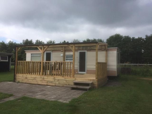 a wooden cabin with a deck on a yard at Stacaravan op camping De Peelweide in Grashoek