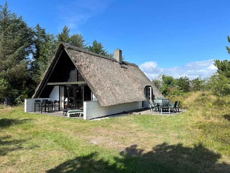 a thatch roofed house with chairs and tables at Charmerende sommerhus in Ringkøbing