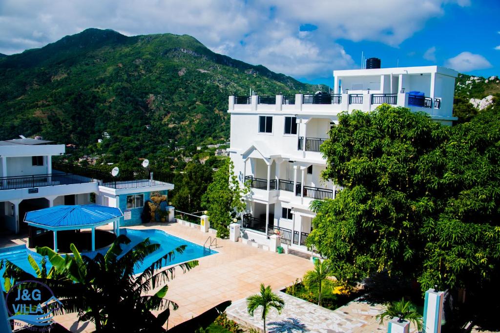 a building with a swimming pool and a mountain at J&G Villa Hotel in Cap-Haïtien