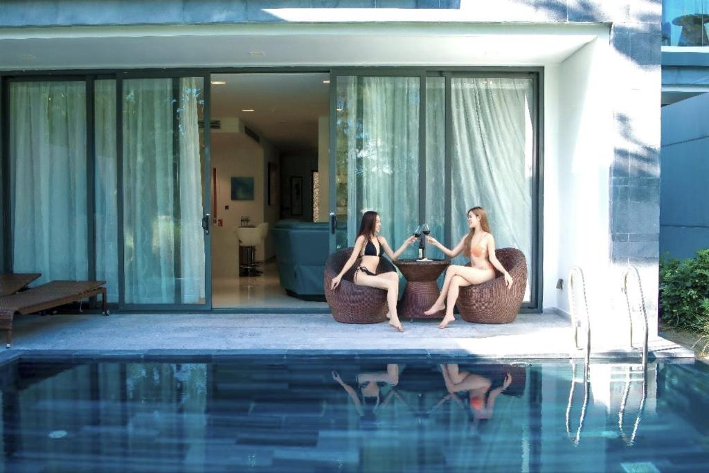 two women sitting on chairs next to a swimming pool at "BRG GOLF CLUB" - Danang Private Pool Villa 3 Bedrooms #2 in Danang