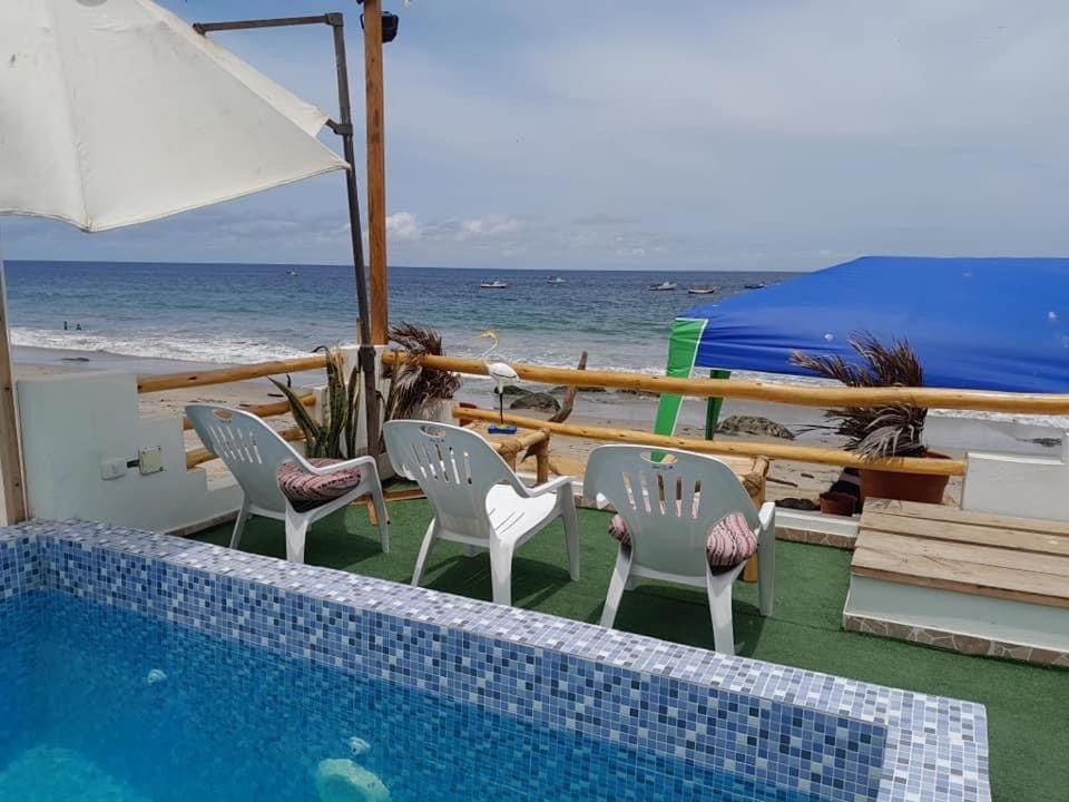 a pool with chairs and an umbrella and the ocean at Hospedaje Casa Mercedes Beach in Canoas De Punta Sal