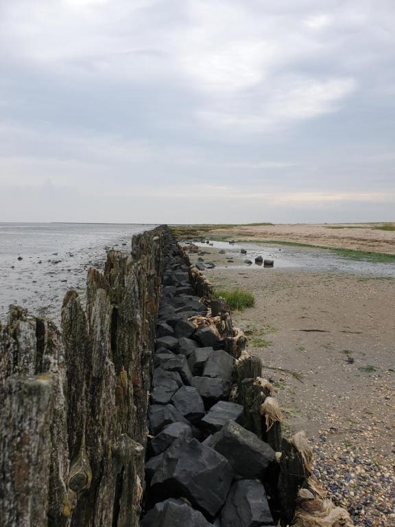 una pared de piedra en una playa junto al agua en De Horizon, slapen in hutten en Kloosterburen