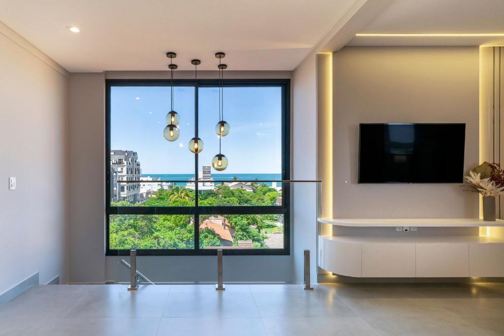 ein Wohnzimmer mit einem großen Fenster und einem Flachbild-TV in der Unterkunft Paradise 205 - Cobertura 2 suítes com vista para o mar de dentro e mar de fora na praia do Canto Grande in Bombinhas