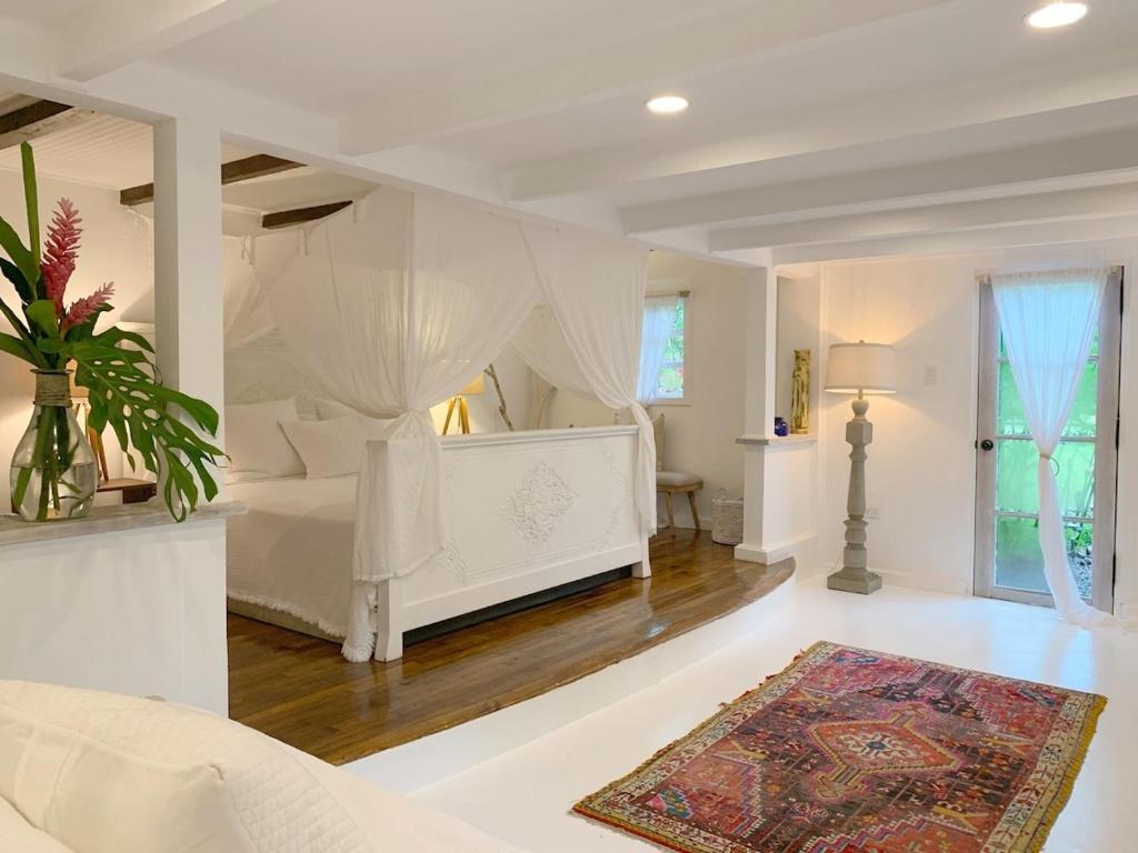 a white bedroom with a white bed and a rug at Monte Sagrado Reserve - wellnessTanama Riverfarm cabin in Quebrada