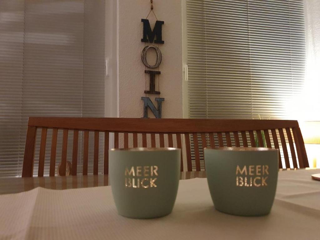 dos tazas sentadas en una mesa delante de un banco en Haus Bremers Hafen, en Borkum