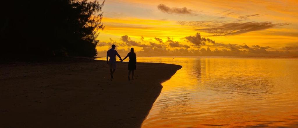 2 personnes marchant sur la plage au coucher du soleil dans l'établissement Resort Tava'e, à Amuri