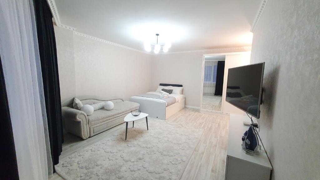 een witte woonkamer met een bank en een tv bij 27 1 комн кв с кондиционером возле Байтерка на 4х человек in Astana