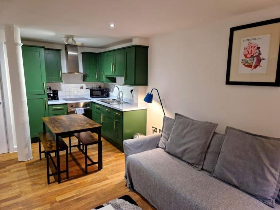 un salon avec un canapé et une cuisine avec des placards verts dans l'établissement Northern Quarter Flat, à Manchester