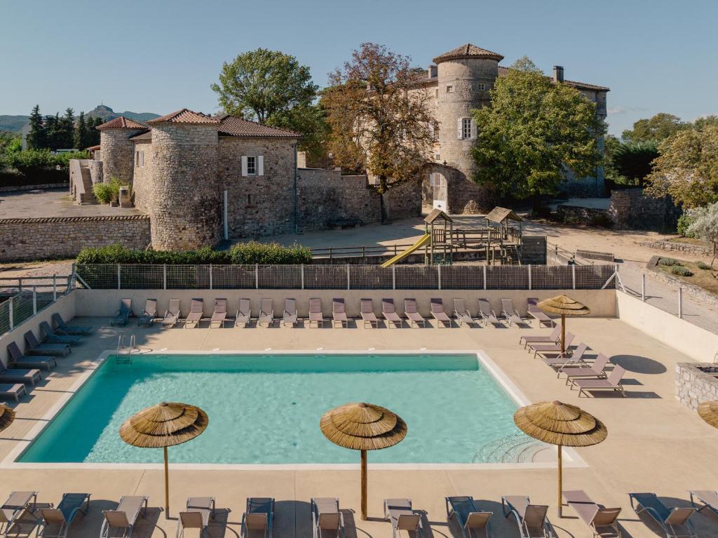 a swimming pool with chairs and umbrellas in front of a castle at Château De Chaussy in Ruoms