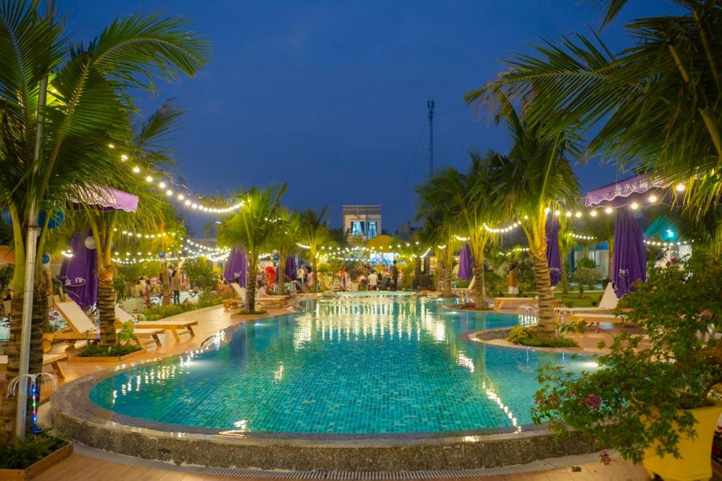 uma grande piscina com luzes e palmeiras à noite em Nhật Hạ Villa em Tam Hà