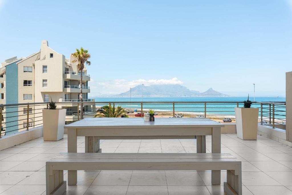 una mesa y bancos en un balcón con vistas al océano en Portico, en Bloubergstrand