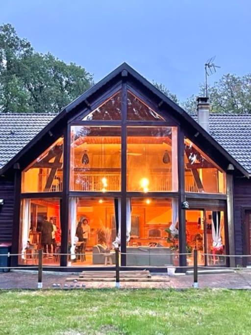 Une grande maison en verre avec des personnes à l'intérieur dans l'établissement Chalet Acacia au calme 1h30 de Paris, à La Selle-en-Hermoy