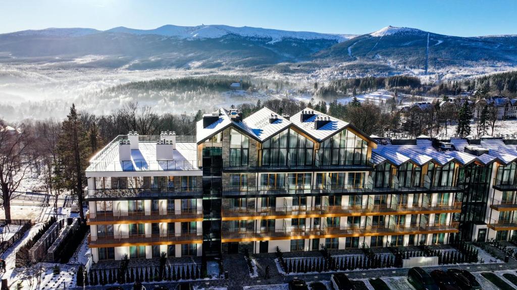 un edificio nella neve con montagne sullo sfondo di Złoty Horyzont Resort Szklarska Poręba a Szklarska Poręba