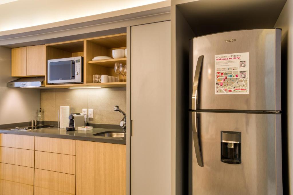 A compact kitchenette with a microwave, sink, coffee setup and full-height refrigerator.
