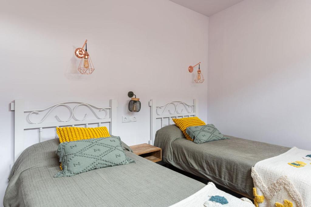 two beds in a room with white walls and yellow pillows at Apartamentos Rurales San Pedro in Valencia de Alcántara