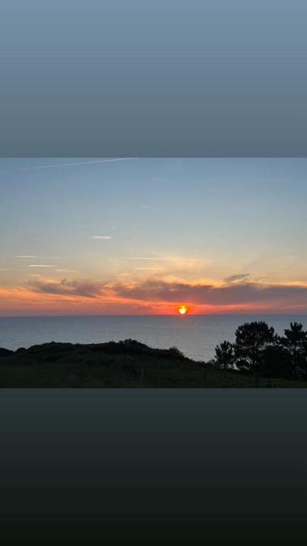 a sunset over the ocean with trees in the foreground at Hotel Restaurante el Fornon in Novellana