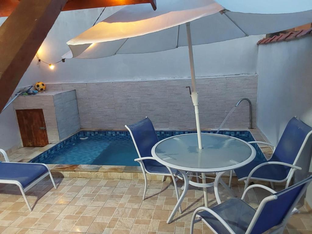 a table with chairs and an umbrella next to a swimming pool at Doce Refugio Itanhaém in Itanhaém