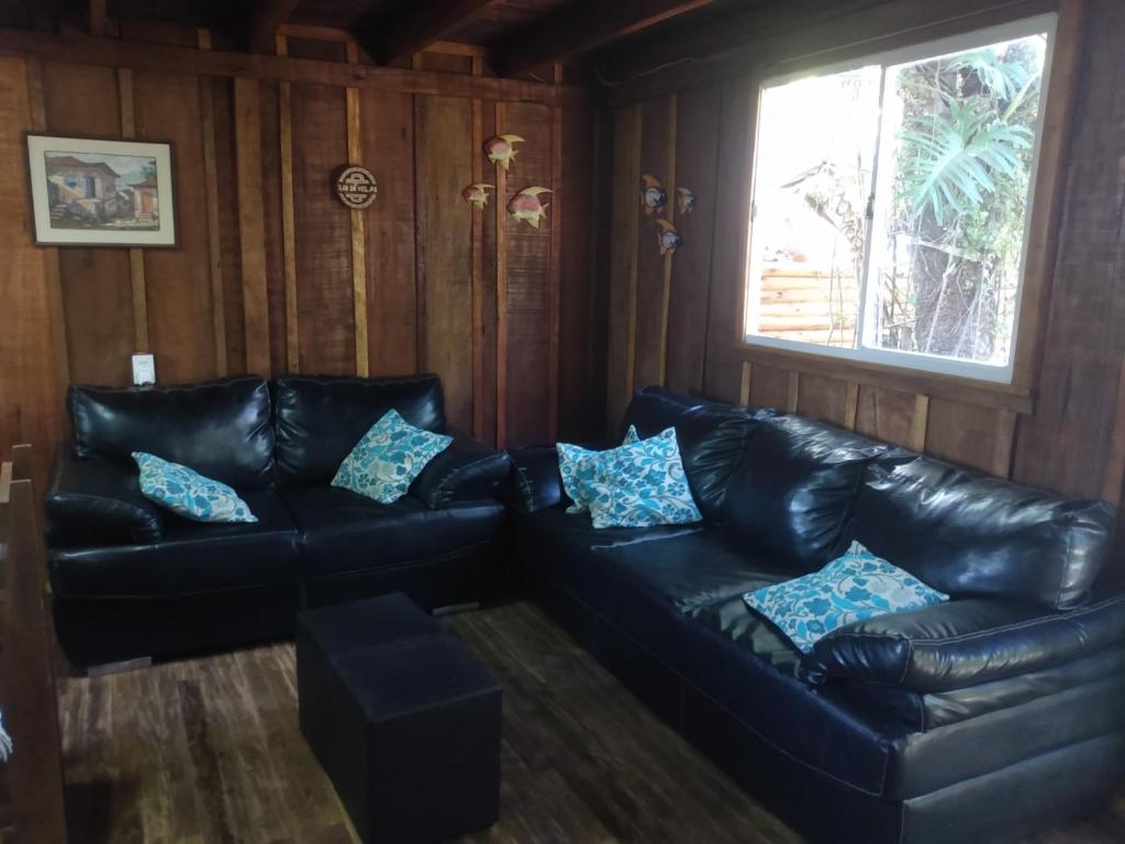 uma sala de estar com sofás de couro preto e uma janela em Casa do Campo na Ilha do Mel