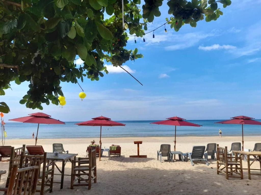 una playa con mesas, sillas y sombrillas rojas en Lanta Mermaid Resort, en Ban Ai Dao