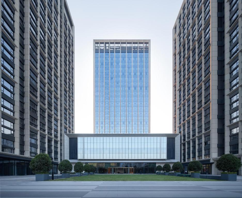 un grand bâtiment en verre au milieu de deux grands bâtiments dans l'établissement Grand New Century Hotel Binjiang Hangzhou, à Hangzhou