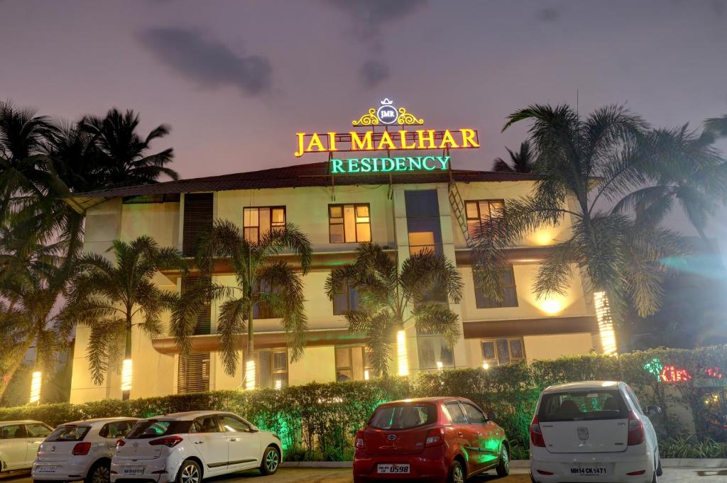 JAI MALHAR RESIDENCY في Kālundri: فندق فيه سيارات تقف امامه