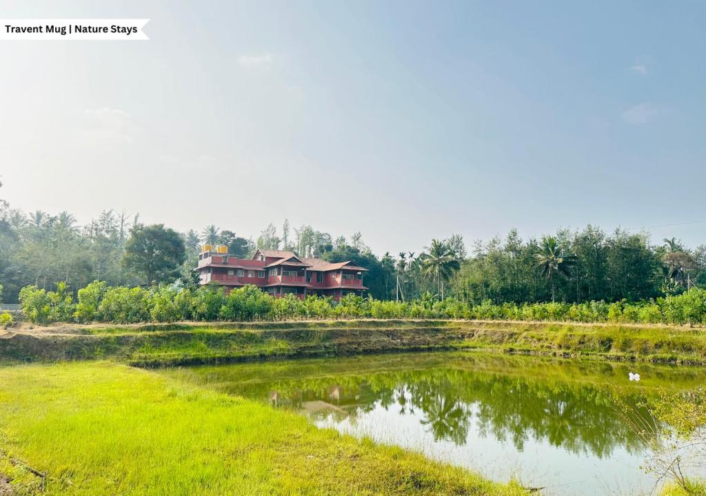 a house in a field next to a river at Pepper Corn Retreat by Travent Mug in Sakleshpur