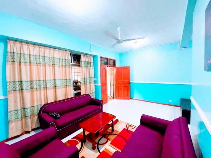 ILHAM HOMESTAY Taman Sejati Mile 7 في سانداكان: غرفة معيشة مع أرائك أرجوانية وطاولة حمراء