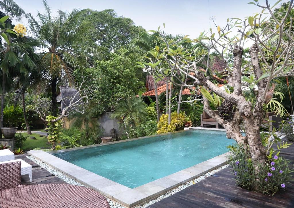 a swimming pool in a garden with a tree at Urbanest Inn Villa in Seminyak