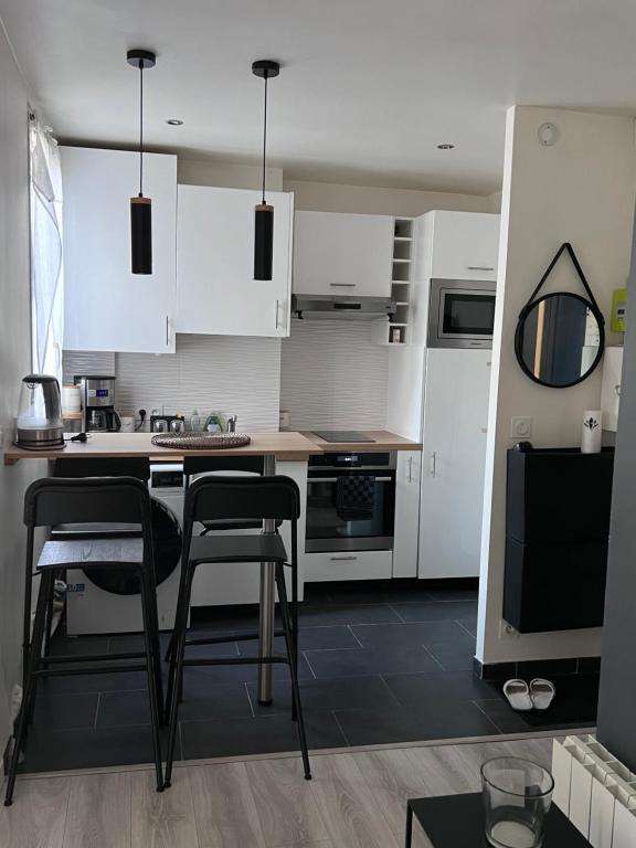 uma cozinha com armários brancos e cadeiras pretas em AUBERVILLIERS COSY em Aubervilliers