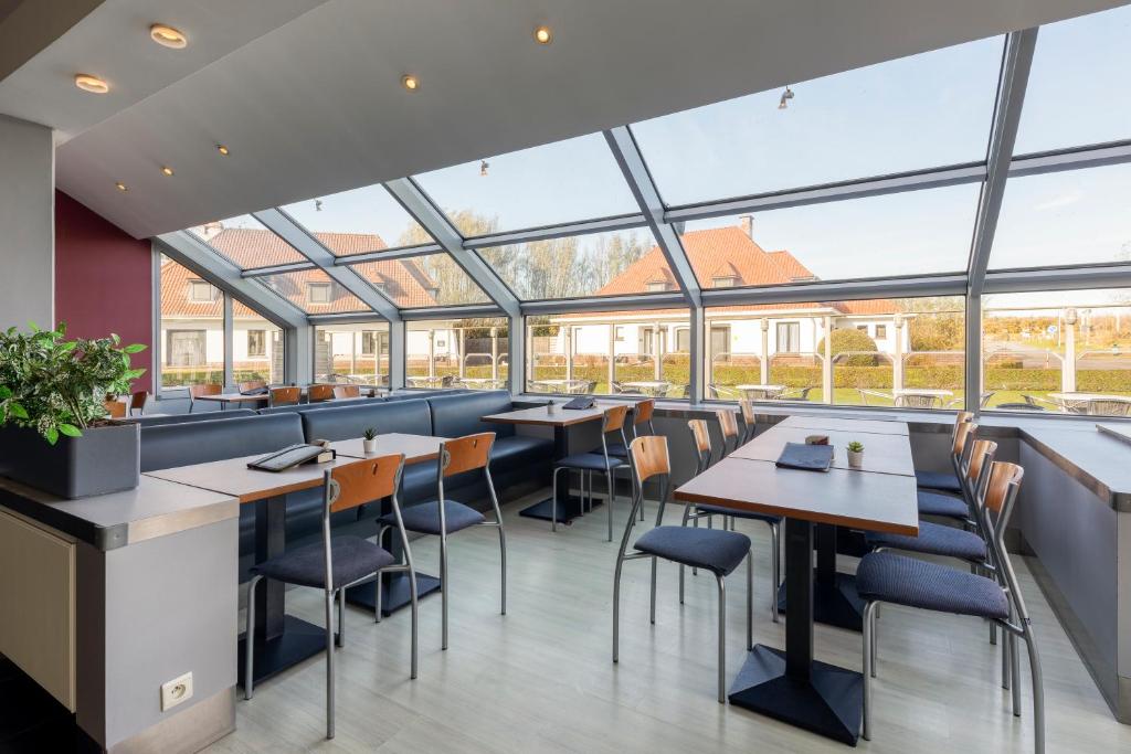 a restaurant with tables and chairs and large windows at Corsendonk Duinse Polders in Blankenberge