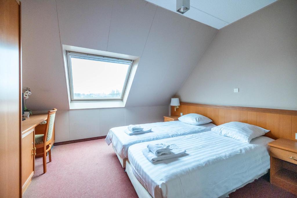 a bedroom with two beds and a desk and a window at Corsendonk Duinse Polders in Blankenberge