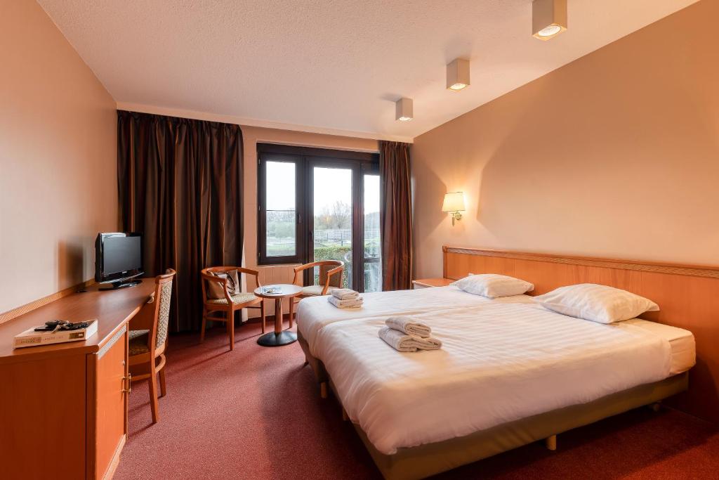 a hotel room with a bed and a desk and a television at Corsendonk Duinse Polders in Blankenberge