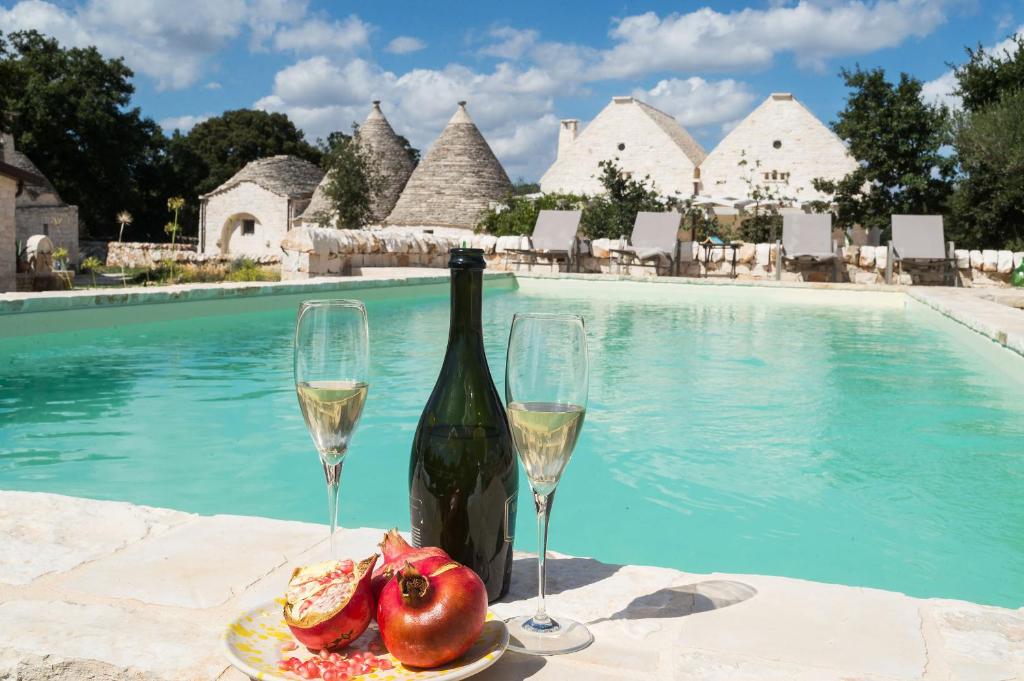 eine Flasche Wein und zwei Gläser neben einem Pool in der Unterkunft Le Dieci Porte in Alberobello