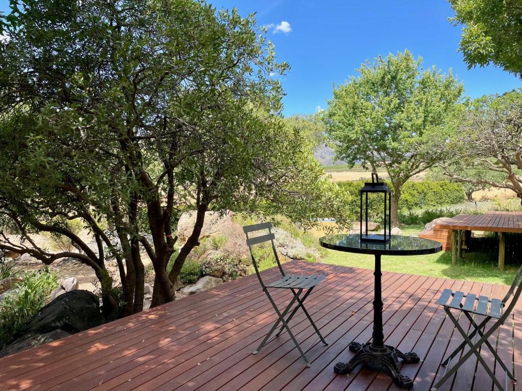 a table and two chairs on a deck with trees at Mountain Cottages at Haskell Vineyard in Stellenbosch