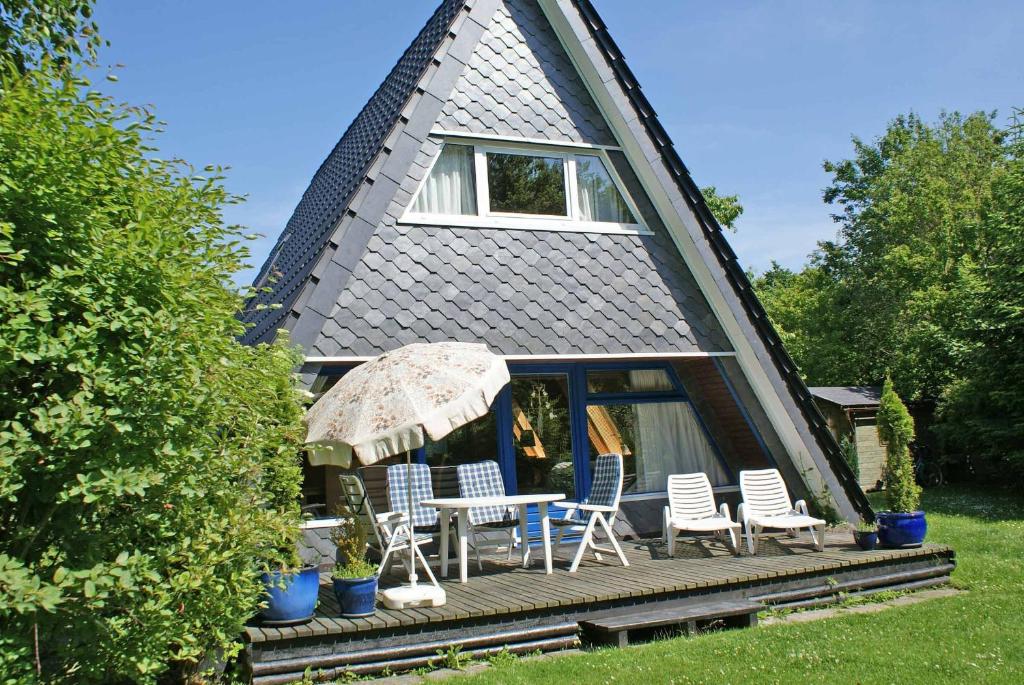 a house with a deck with chairs and an umbrella at Zeltdachhaus mit Kamin und grosser Terrasse in Damp