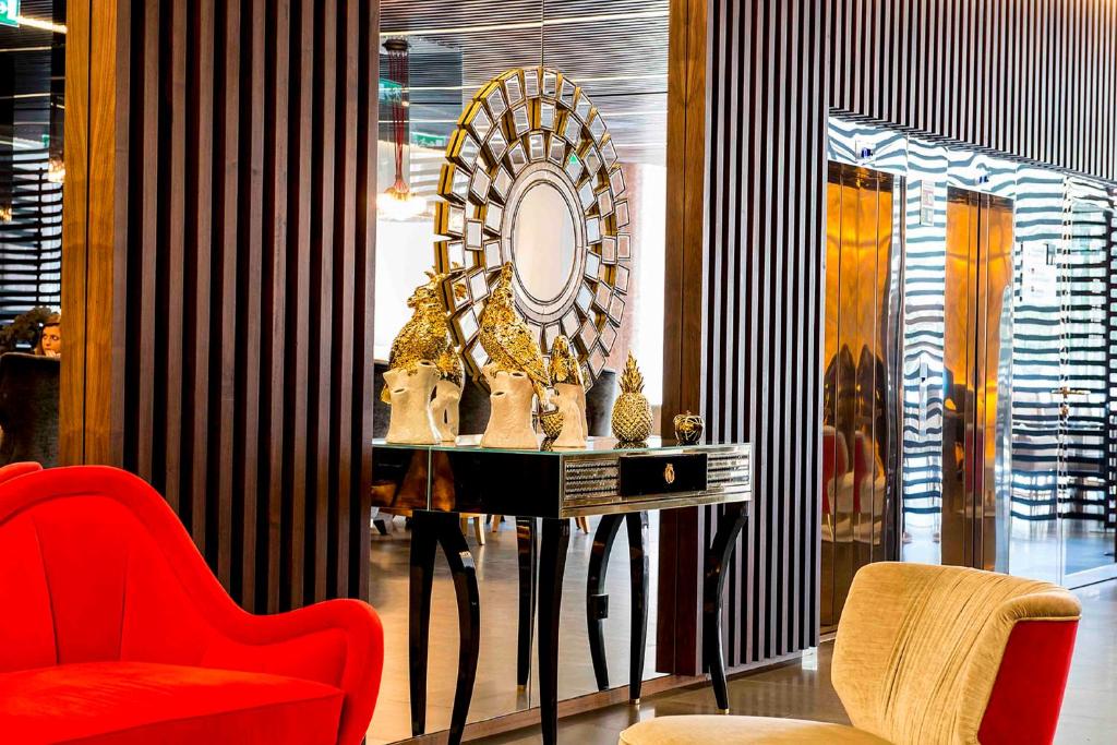 A richly styled seating corner with a red armchair, console table and decorative mirror.