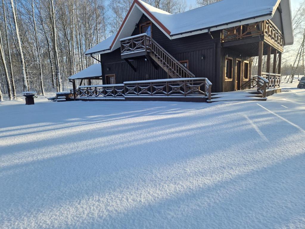 Cabaña de madera con nieve en el suelo en Piligrimo sodyba, en Kadarės