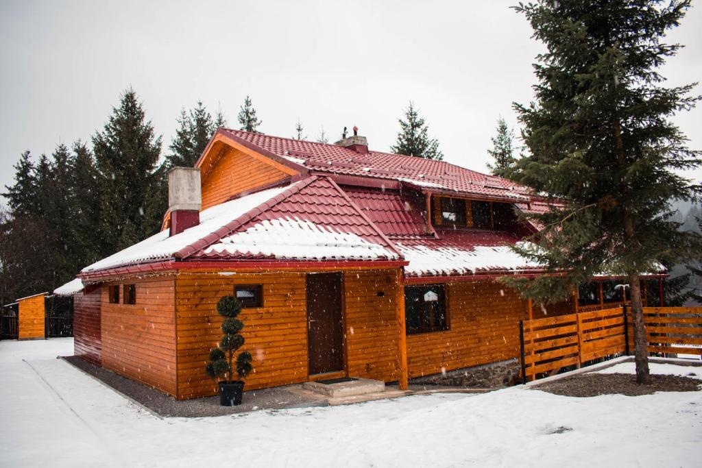 une maison en bois avec de la neige sur le toit dans l'établissement Cabana Stînă, à Topliţa