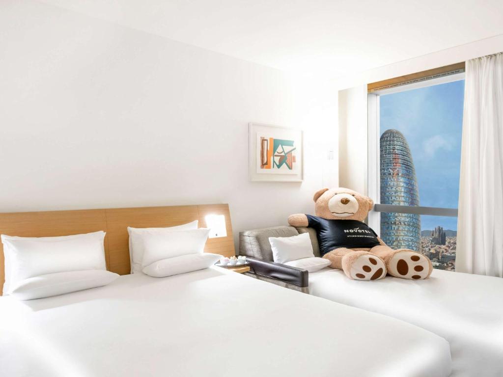 a hotel room with two beds with a teddy bear at Novotel Barcelona City in Barcelona