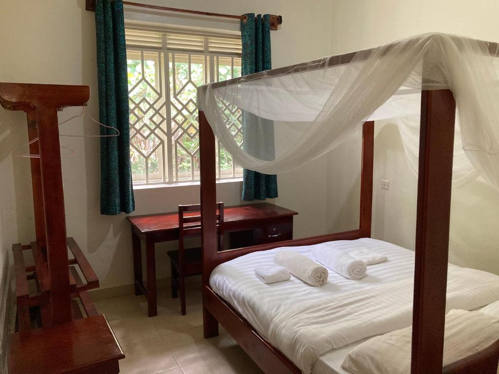 a bedroom with a bed and a desk and a window at Bwindi Guest House in Kinkizi