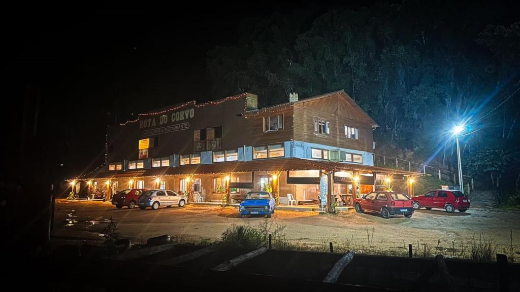a building with cars parked in a parking lot at night at Pousada Rota do Corvo - Grão-Pará - SC in Grão Pará